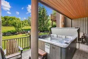 Un bain à remous sur une terrasse en bois, avec vue sur une zone herbeuse et des arbres.