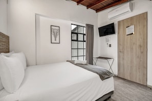 A bedroom with a bed, a window, a TV, and a wooden door. - Encanto House in Provenza by Nowa (Medellín)