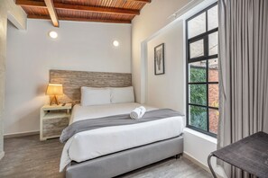 A bedroom with a bed, bedside table, lamp, window, and curtains. - Encanto House in Provenza by Nowa (Medellín)
