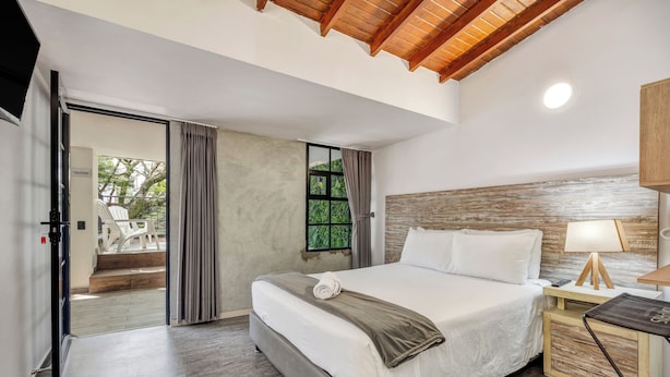 Un dormitorio con cama, mesita de noche, lámpara, ventana con cortinas y vista a un espacio exterior.