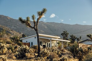 Ein modernes Haus mit Terrasse, umgeben von Wüstenpflanzen und Bergen.