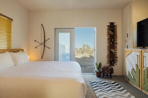 A bedroom with a large bed, a door leading to a balcony, and a television on a wooden cabinet. - Romantic Desert Oasis, Hot Tub, Stargazing, 10 Min to JTNP! (Joshua Tree)