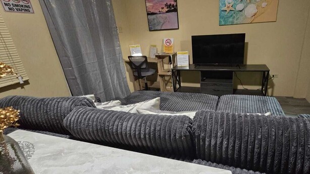 Ein Zimmer mit einer großen Couch, einem Schreibtisch mit Stuhl, einem Fernseher und einem Bett.