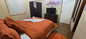 Ein Schlafzimmer mit Bett, Kommode, Fernseher und Tür.