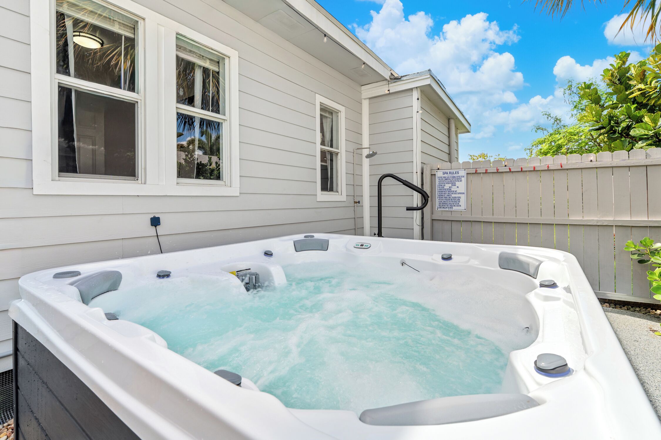 A hot tub outside a house with a wooden fence and a sign.