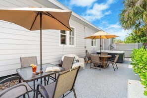 Eine Terrasse mit Gartenmöbeln, einem Tisch mit Buch und Getränk sowie Sonnenschirmen.