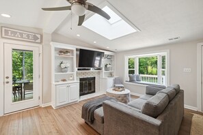 Ein modernes Wohnzimmer mit Kamin, Deckenventilator und Blick ins Freie.