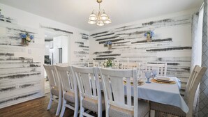 A dining area with a white table set for six, white chairs, a chandelier, and a rustic wall design.