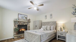 A bedroom with a stone fireplace, a bed with a headboard, a nightstand, and a ceiling fan.