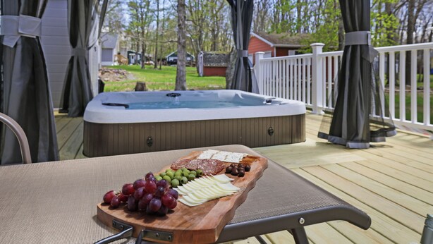 A hot tub on a wooden deck with a wooden board displaying cheese, grapes, and olives.