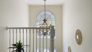 A staircase with a white railing, a chandelier, and a large arched window with a view of trees.