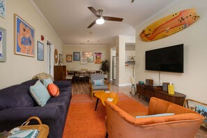 A living room with a sofa, armchair, TV, ceiling fan, and artwork on the walls. - Stylish Retreat Close to Dining and Outlets, Minutes to Beach (Rehoboth Beach)