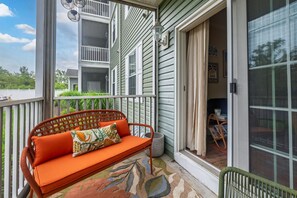 A porch with a wicker sofa, a small table, and a window with a view of a house. - Stylish Retreat Close to Dining and Outlets, Minutes to Beach (Rehoboth Beach)