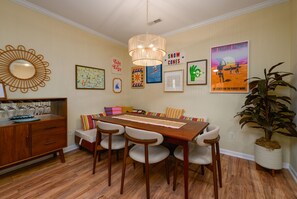 A dining area with a wooden table, chairs, a chandelier, and wall art. - Stylish Retreat Close to Dining and Outlets, Minutes to Beach (Rehoboth Beach)