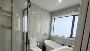 A modern bathroom with a glass-enclosed shower, a toilet, a bathtub, and a large window providing natural light. - Modern Family Home in Tawa. 
Pet Friendly Property (Wellington)