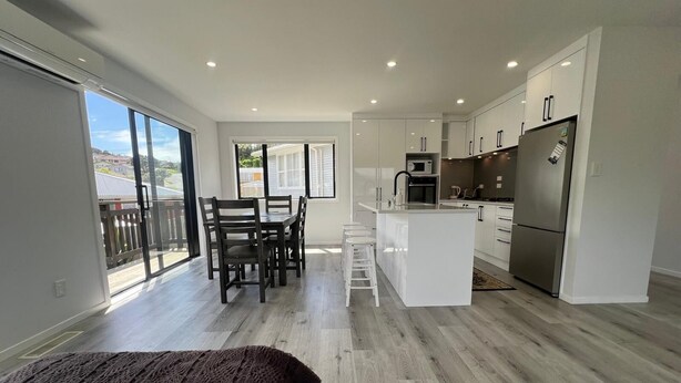 A modern kitchen with a central island, a dining area with chairs, and a large sliding glass door leading to a balcony. - Modern Family Home in Tawa. 
Pet Friendly Property (Wellington)