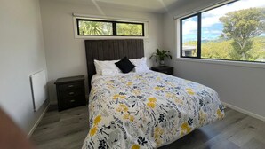 A bedroom with a bed, a nightstand, a potted plant, and a window with a view of trees. - Modern Family Home in Tawa. 
Pet Friendly Property (Wellington)