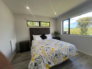 A bedroom with a bed, a nightstand, a potted plant, and a window with a view of trees. - Modern Family Home in Tawa. 
Pet Friendly Property (Wellington)