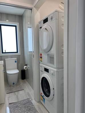 A compact laundry room with a washing machine, dryer, and toilet. - Modern Family Home in Tawa. 
Pet Friendly Property (Wellington)