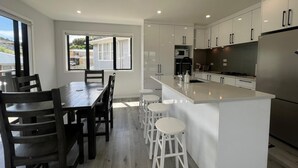 A modern kitchen with white cabinetry, a central island with stools, a dining table with chairs, and a view through a window. - Modern Family Home in Tawa. 
Pet Friendly Property (Wellington)