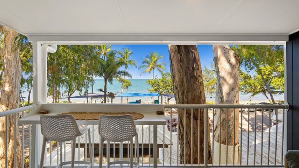 A balcony with a view of the beach, palm trees, and a clear sky. - Relaxing Beachfront Palm Cove Studio with Ocean Views, Pool Access & Walkable Dining (Palm Cove)