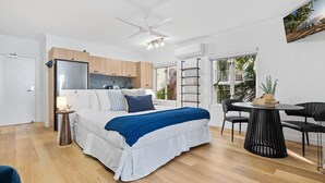 A bedroom with a bed, bedside table, lamp, and a view of the kitchen and outside. - Relaxing Beachfront Palm Cove Studio with Ocean Views, Pool Access & Walkable Dining (Palm Cove)