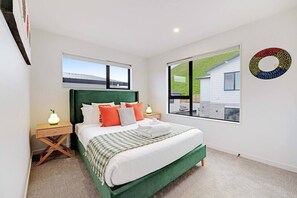 A bedroom with a bed, a nightstand, a lamp, a window with a view, and a wall decoration.