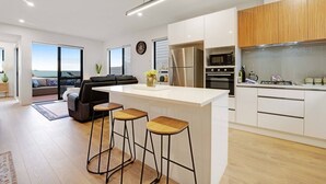 A modern kitchen with a central island, bar stools, and a view to the outdoors. - Spacious 4BR Family Haven with Air-con & Parking (Auckland South)