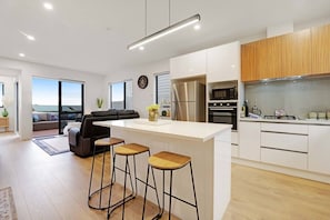 A modern kitchen with a central island, bar stools, and a view to the outdoors. - Spacious 4BR Family Haven with Air-con & Parking (Auckland South)