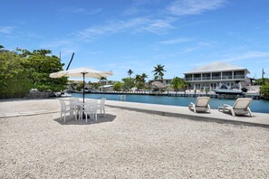A poolside area with lounge chairs, a table, and umbrellas. - Port Palermo - Canal Home w/Dockage, Pet Friendly! (Islamorada)