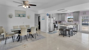 Een moderne keuken met een centraal eiland, een eethoek met een tafel en stoelen, en een plafondventilator.