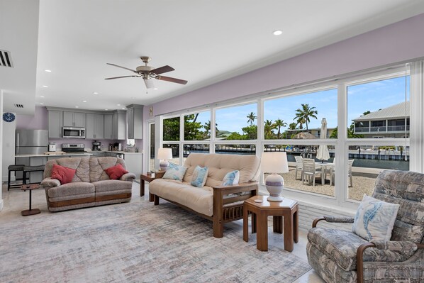 A spacious living area with a sofa, armchair, and coffee table, a kitchen with modern appliances, and large windows offering a view of the beach and ocean. - Port Palermo - Canal Home w/Dockage, Pet Friendly! (Islamorada)