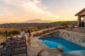 Une piscine bordée de murs en pierre, dotée de chaises longues et offrant une vue sur les montagnes.