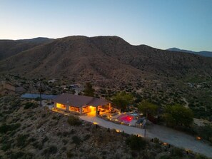 A single-story building with a patio area, surrounded by a desert landscape with hills in the background.