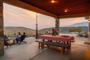 An outdoor patio with a stone wall, a table with a checkered tablecloth, and a fire pit.