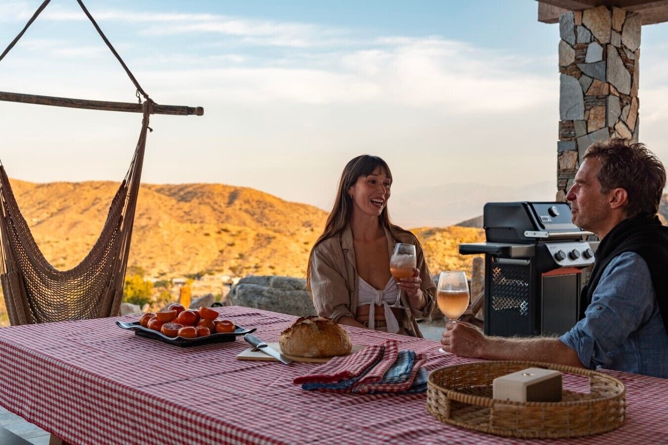 Un couple dînant en plein air, près d’un barbecue, d’un hamac, avec une vue sur les collines.