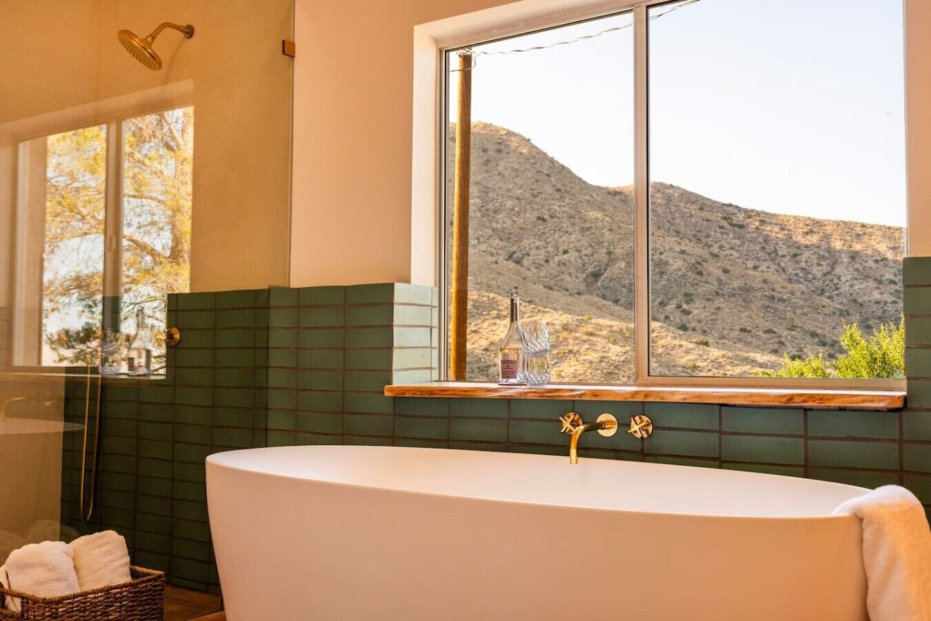 Un baño con una bañera independiente, una ventana con vista a un paisaje montañoso y una pared de azulejos verdes.