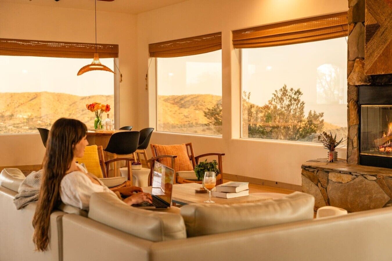A cozy living room with a fireplace, a sofa, a dining table with chairs, and a view of the outdoors.