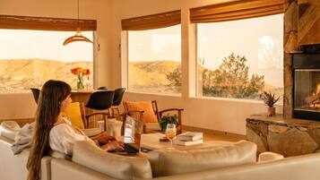 A cozy living room with a fireplace, a sofa, a dining table with chairs, and a view of the outdoors.