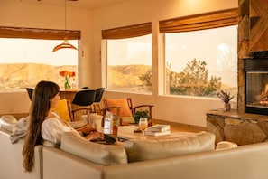 A cozy living room with a fireplace, a sofa, a dining table with chairs, and a view of the outdoors.