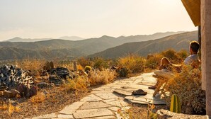 A stone pathway leading through a natural landscape with cacti and dry grass, overlooking a mountainous area. - Casa Sole | Pool | Spa | Near Palm Springs (Morongo Valley)