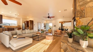 A spacious living room with a large sofa, coffee table, and chairs, a stone fireplace, and a view of the mountains. - Casa Sole | Pool | Spa | Near Palm Springs (Morongo Valley)