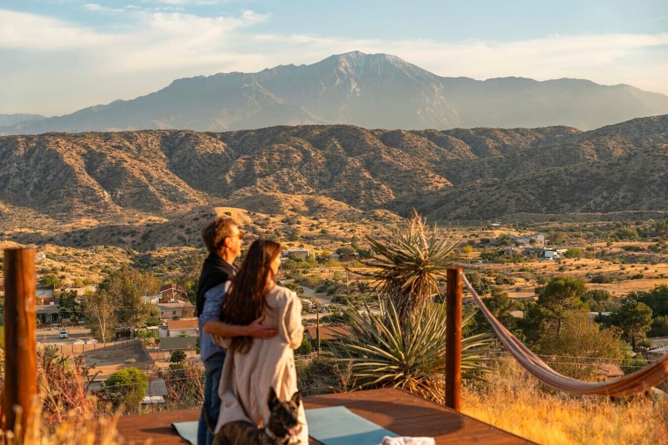 A couple embracing on a wooden deck with a view of a mountainous landscape.