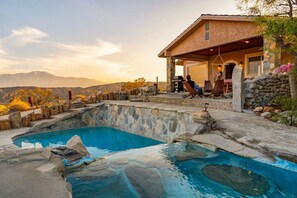 Une piscine bordée de pierres, un patio couvert et une vue sur les montagnes.