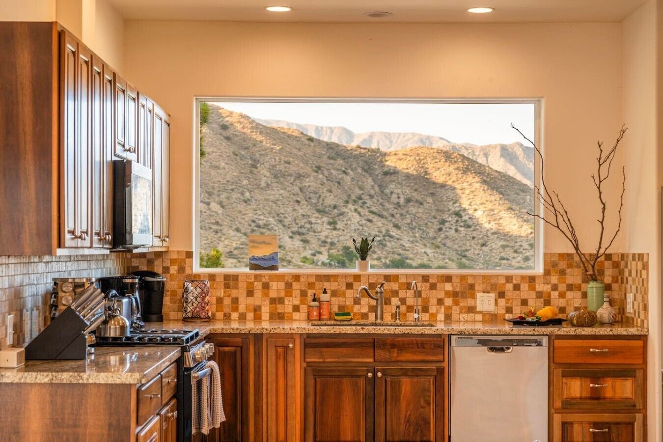 A kitchen with wooden cabinets, a large window with a mountain view, and a tiled backsplash.