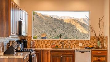 A kitchen with wooden cabinets, a large window with a mountain view, and a tiled backsplash.