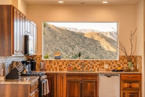 A kitchen with wooden cabinets, a large window with a mountain view, and a tiled backsplash.