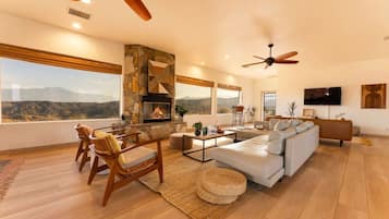 A spacious living room with a fireplace, large windows, and a view of the mountains.