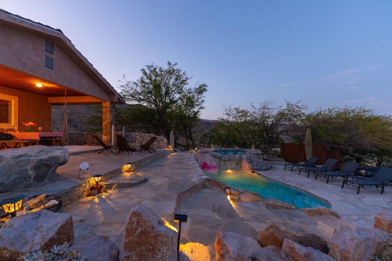 A pool area with stone steps, lounge chairs, and a dining setup.