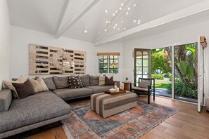 A modern living room with a sectional sofa, a patterned rug, and a large abstract wall art piece. - NEW Montecito Hedgerow Jewel Box, 4BD/3BA, with Pool and Jacuzzi! (Santa Barbara)